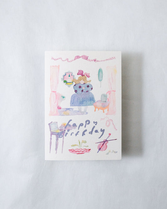 A square greeting card featuring a whimsical watercolor illustration of a blue bear wearing a pink bow and crown, surrounded by pastel pink and purple details, with the word 'happi' and 'rday' written in a playful script. The card is photographed flat against a light gray textured background, dodolulu, birthday, card, cute, nz, 