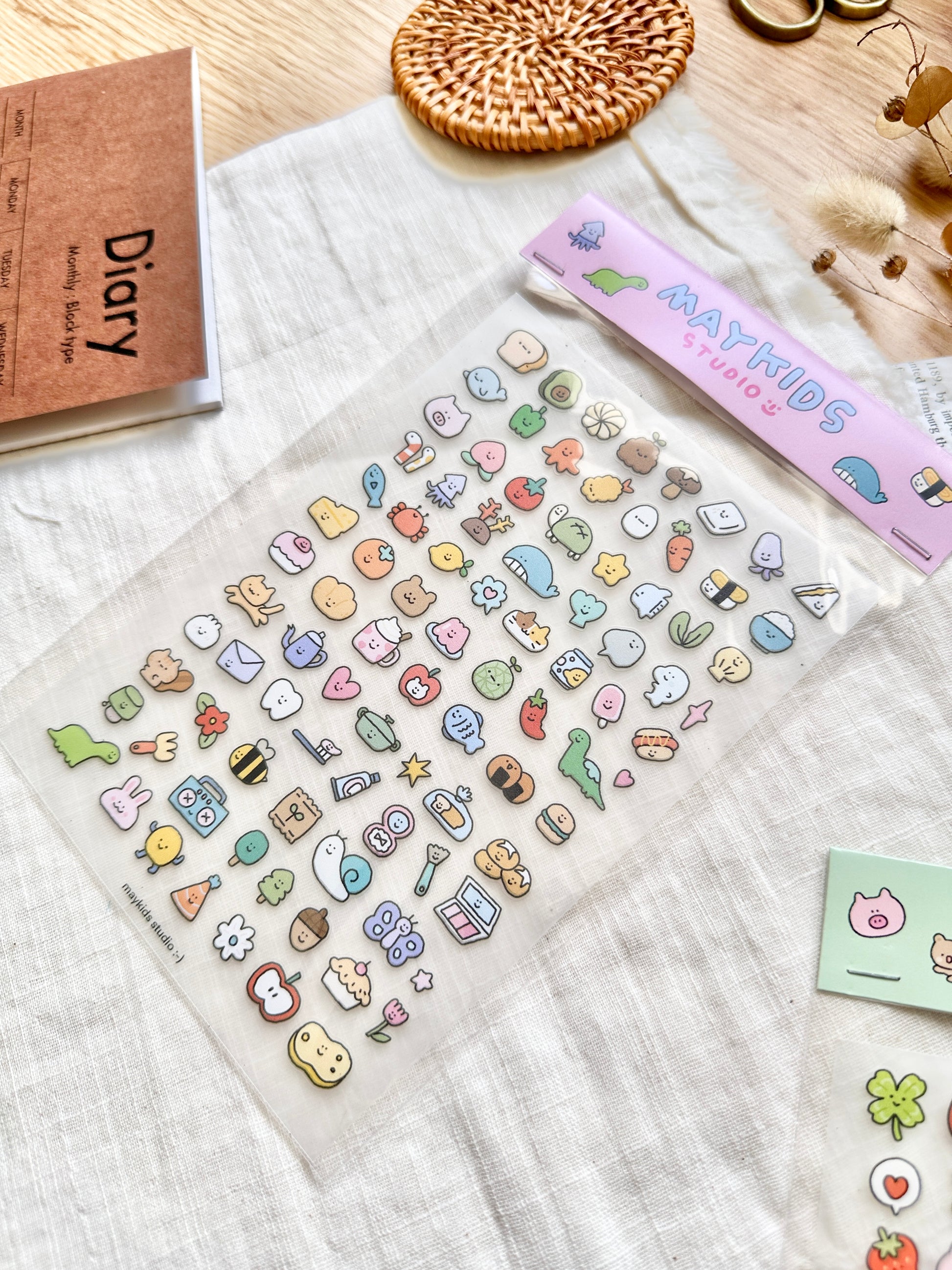 Sheet of colorful stickers with 'MAYKIDS' branding on a textured surface, cute, stickers, hope and letters, nz, dinasour, apple, sushi