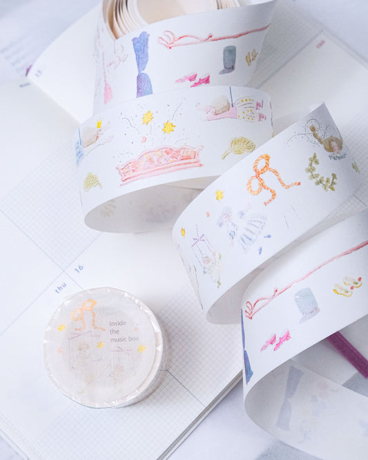 Several rolls of decorative washi tape with pastel illustrations are arranged on an open notebook. The tape features whimsical drawings including a pink sofa, ribbon bows, flowers, and small objects in soft pastel colors like pink, blue, yellow, and green. dodolulu, cute, washi tape