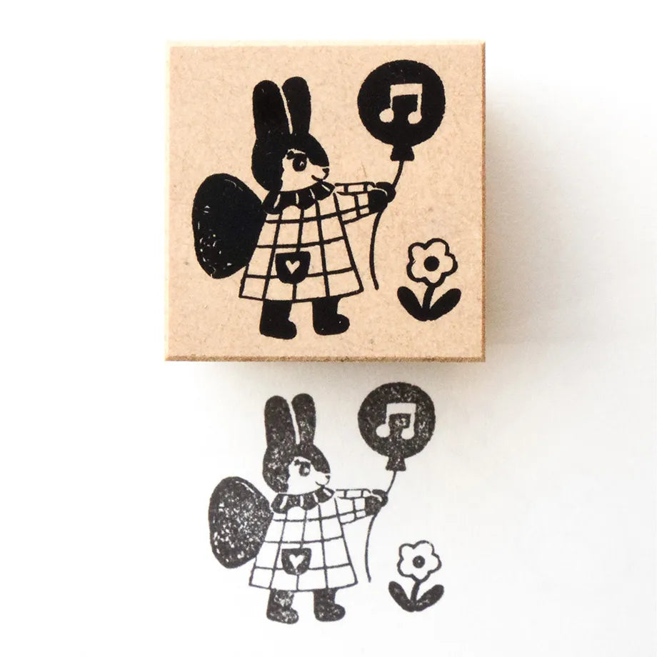 Rubber stamp with a black and white illustration of a rabbit character holding a balloon on a beige background.