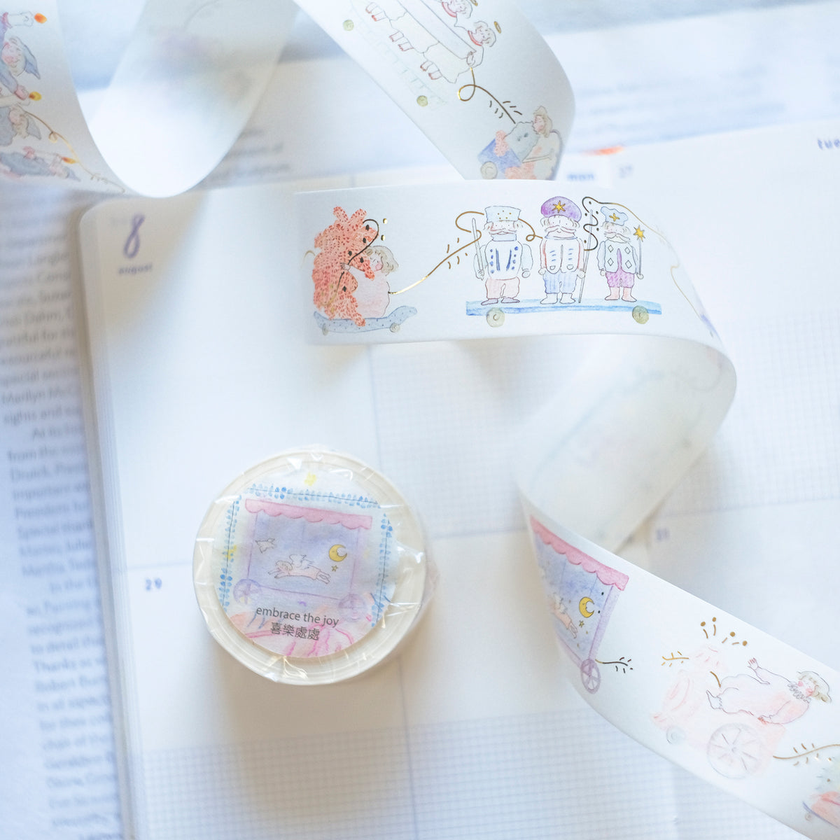 A roll of decorative washi tape with pastel cartoon illustrations and Japanese text, shown unrolled across an open notebook next to the tape roll in plastic wrapping. dodolulu, tape, sticker, cute, pink, washi tape, hope and letters, nz