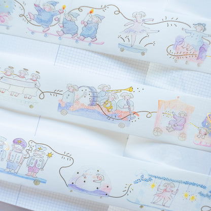 Several rolls of decorative washi tape with whimsical pastel illustrations are arranged diagonally on a white grid notebook. The designs feature cute characters in a train, space, and fairy-themed scenes in soft pastel colors.
