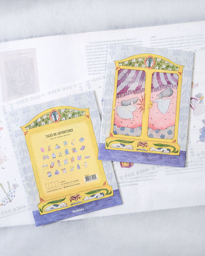 Two illustrated postcards or bookmarks featuring whimsical window scenes and a yellow card titled 'TALES OF ADVENTURES', arranged on top of an open book.
