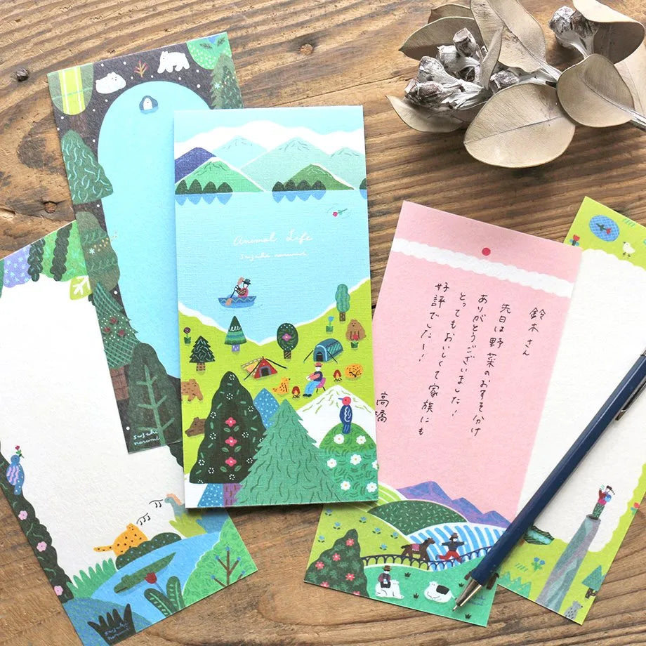 Set of colorful illustrated notebooks on a wooden surface with a pen and decorative elements. Notebook with a colorful illustration of a scenic landscape on a wooden surface, memopad, animal, camping, notepad, nz, hope and letters, cute, japan, mountain, ocean, kayak