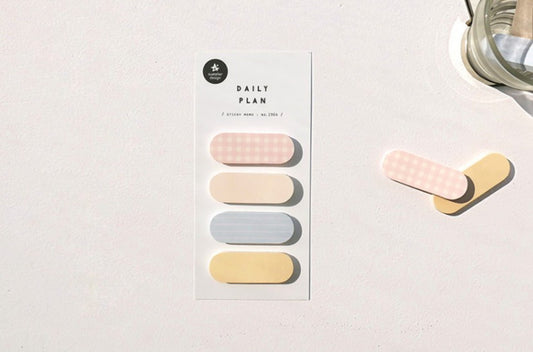 A vertical card labeled 'DAILY PLAN 50' with four pastel pill-shaped tabs in pink, cream, light blue, and pale yellow, placed on a white surface beside two loose matching tabs and part of a glass object. suatelier, korea, nz, hope and letters, sticky notes, memo, cute