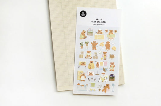 A sheet of cute teddy bear planner stickers labeled 'Ggumi home' lies on top of a beige lined notepad against a clean white background. suatelier, korea, nz, stationery, cute, bear