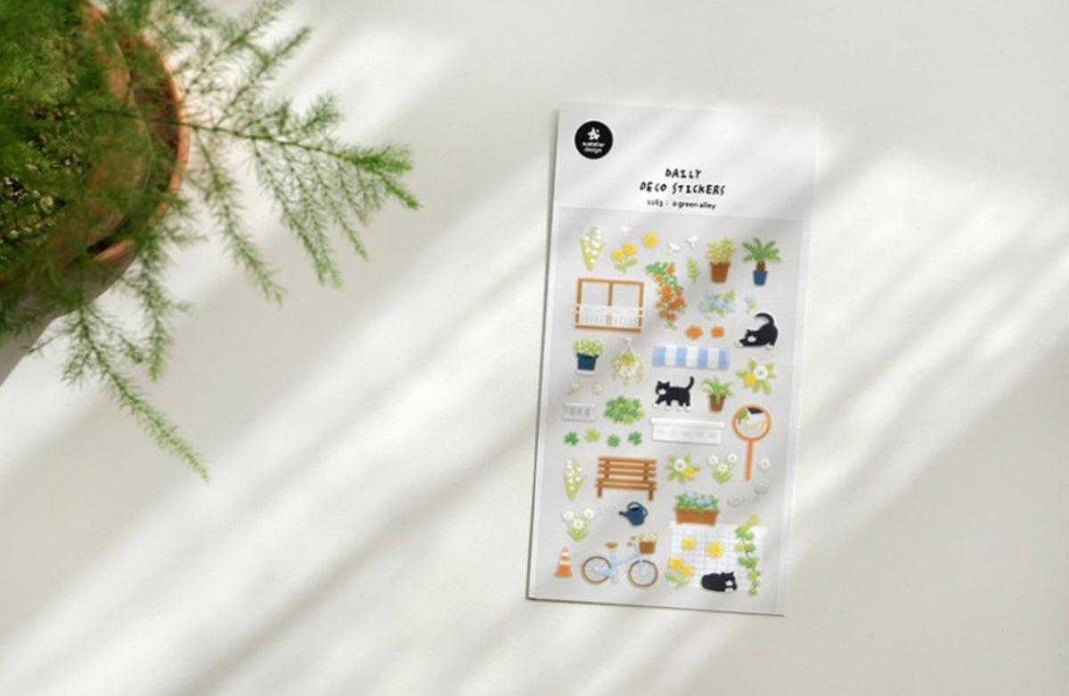 A sheet of cute garden-themed planner stickers displayed on a white surface with soft diagonal shadows, next to a potted green plant. suatelier. nz. cat