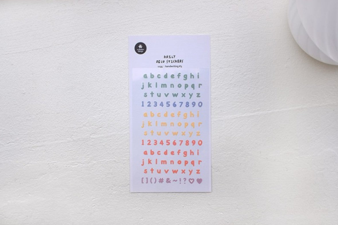 A sheet of alphabet and number stickers in pastel colors, displayed on a textured off-white surface.