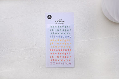 A sheet of alphabet and number stickers in pastel colors, displayed on a textured off-white surface.