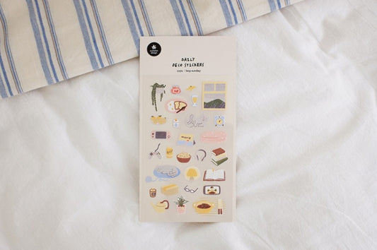 A sheet of cute, minimalist daily food planner stickers displayed on a white bed next to a blue and white striped pillow. The sheet features illustrations of various snacks, drinks, and breakfast items in soft pastel colors. suatelier, stickers, nz, hope and letters